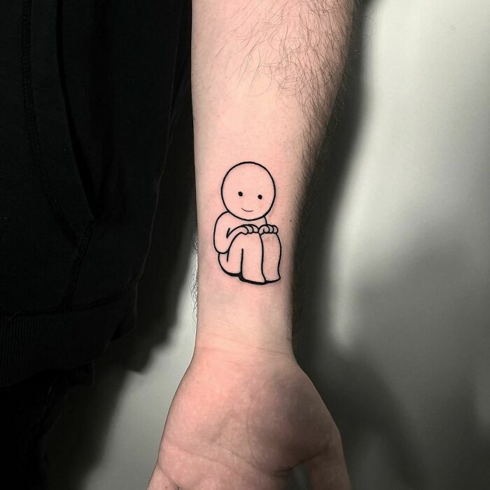 Simple line drawing tattoo of a smiling figure on a forearm, symbolizing mental health healing.