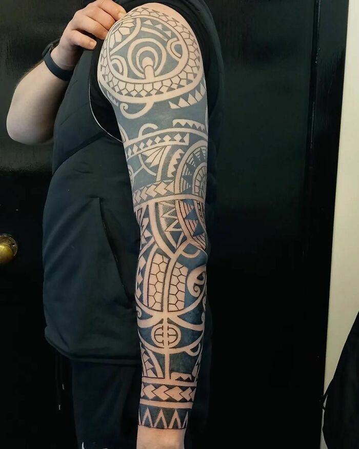 Full sleeve tribal tattoo in intricate black and white design on an arm.