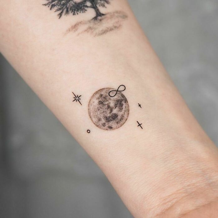 Infinity tattoo on wrist featuring a moon and small celestial symbols.