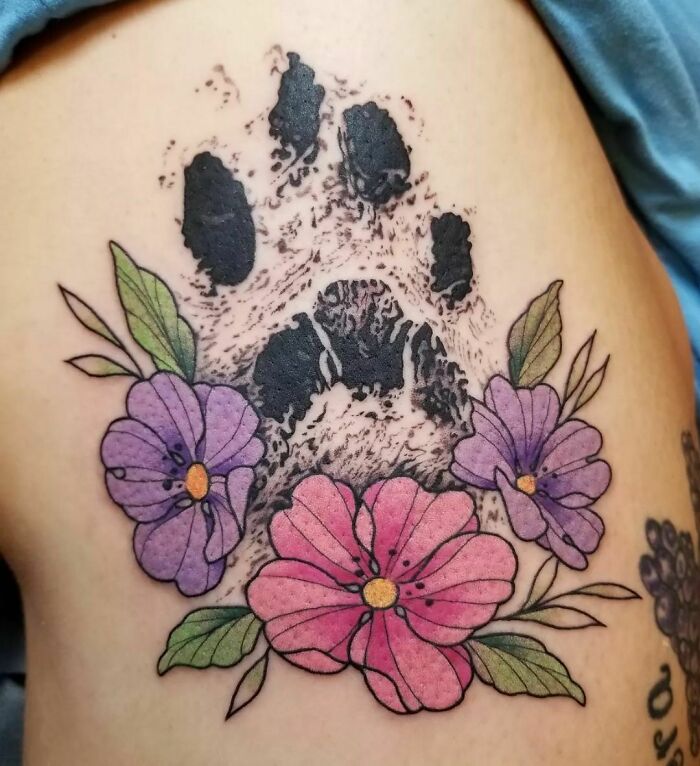 Paw print tattoo with colorful flowers, a memorial design to honor family.