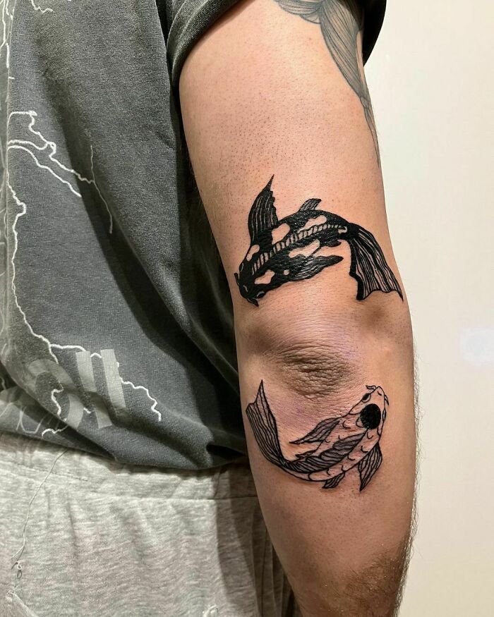 Arm with Yin Yang tattoos featuring two koi fish, symbolizing duality.