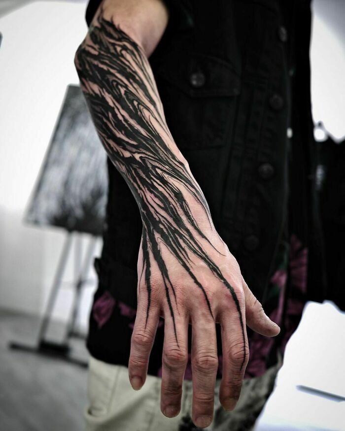 Gothic tattoo with intricate black lines on a person's forearm against a blurred background.