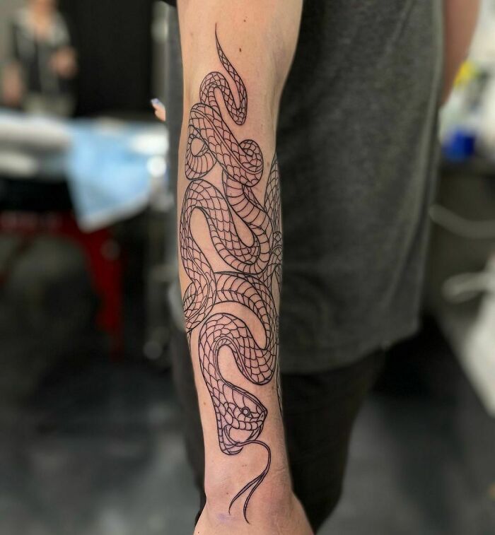 Arm tattoo of an intricately designed snake wrapping around forearm in black ink.