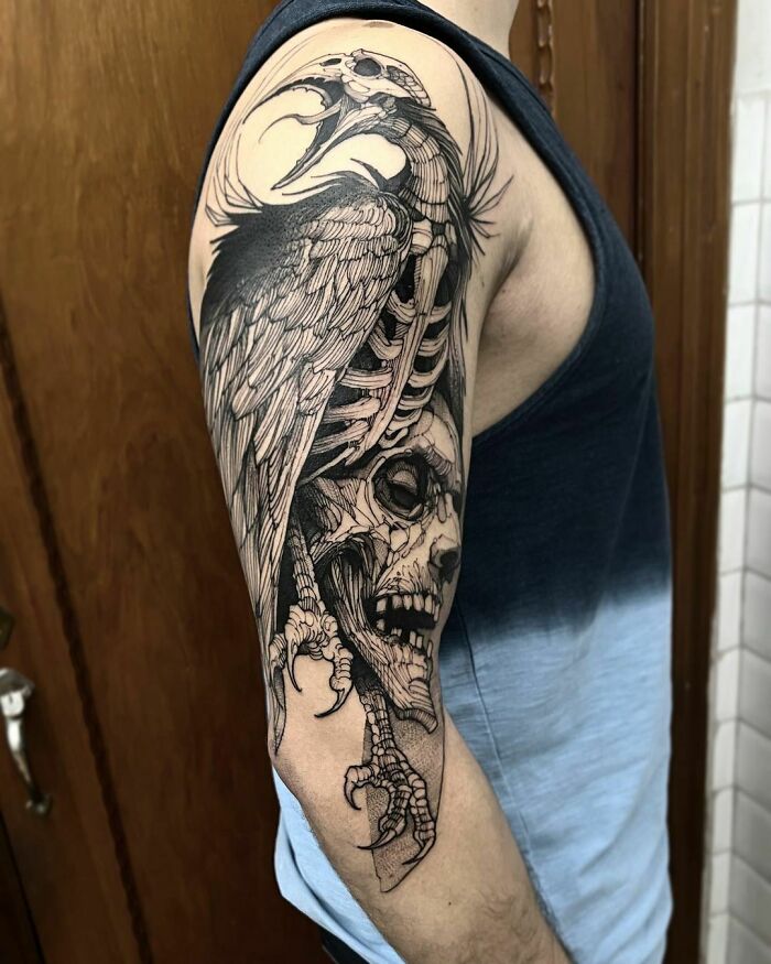 Gothic tattoo on a man's arm featuring a skeletal bird entwined with a human skull, showcasing intricate black ink detail.