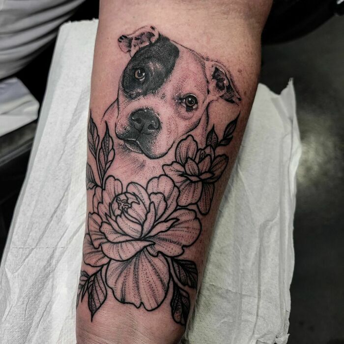 Dog portrait tattoo with flowers on forearm honoring family.