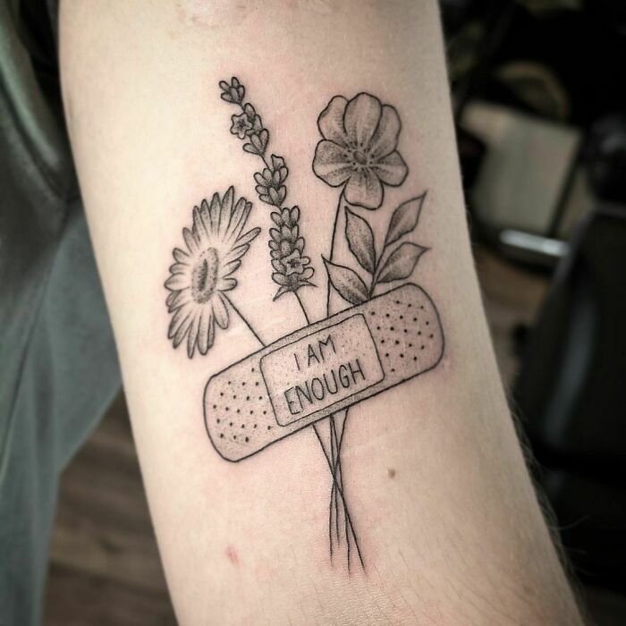 Powerful mental health tattoo with flowers and a band-aid reading "I am enough" on an arm.