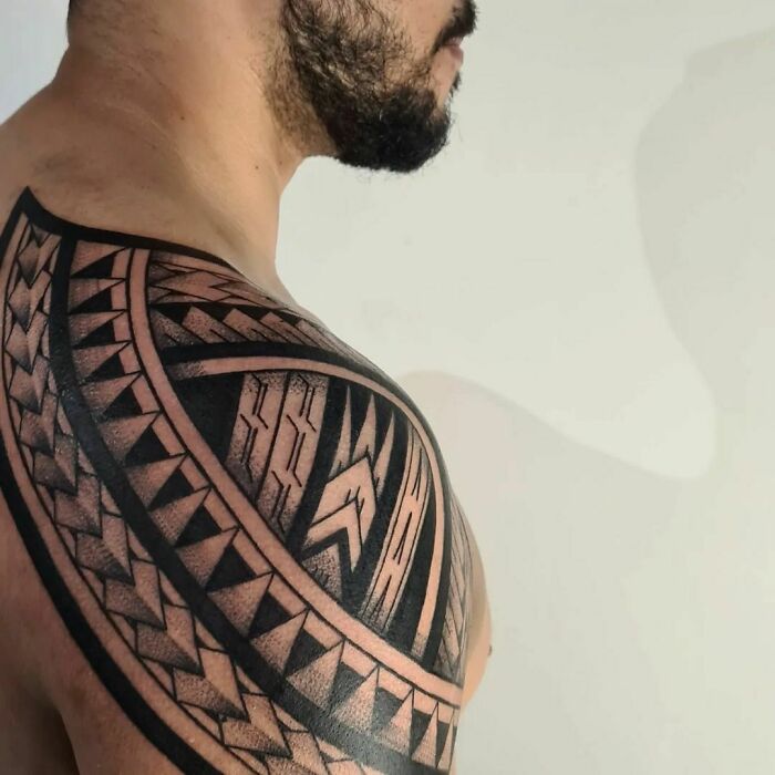 "Man with intricate tribal tattoo design on shoulder, showcasing bold geometric patterns."