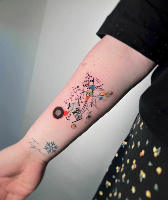 Abstract tattoo on forearm featuring geometric shapes and colorful designs, showcasing artistry and self-expression.