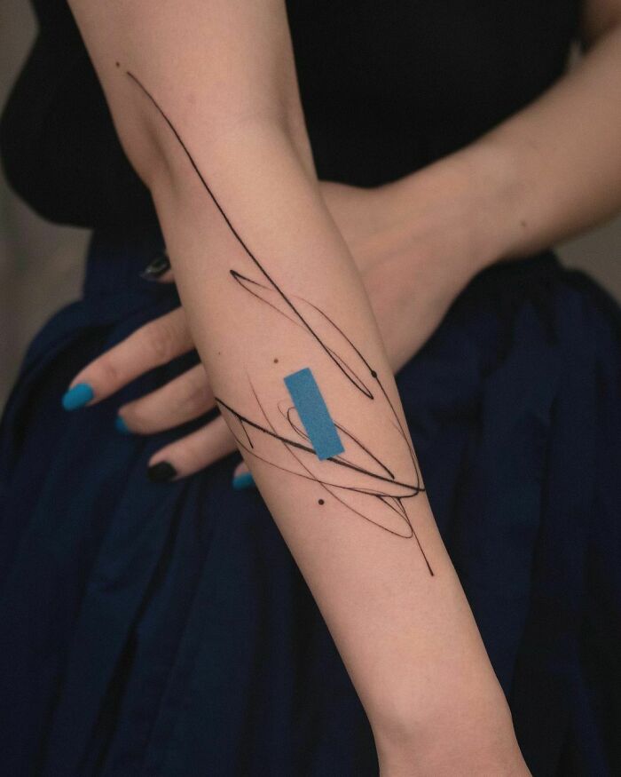 Abstract tattoo with black lines and blue accent on forearm, showcasing artistry and self-expression.