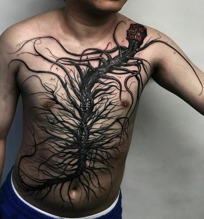A detailed gothic tattoo with black tendrils and red eyes covering a person's chest.