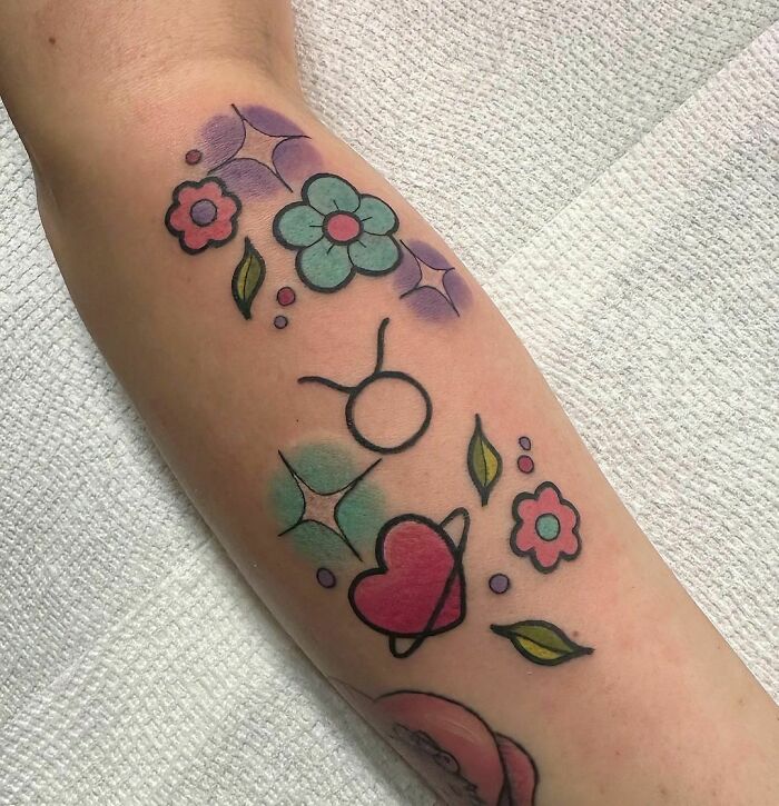 Colorful zodiac tattoo on arm with Taurus symbol, flowers, and hearts.