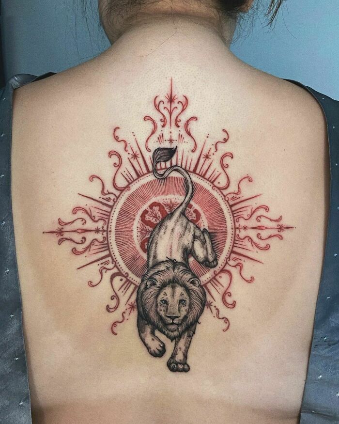 Back tattoo of a detailed lion representing the zodiac sign Leo, surrounded by intricate red designs.
