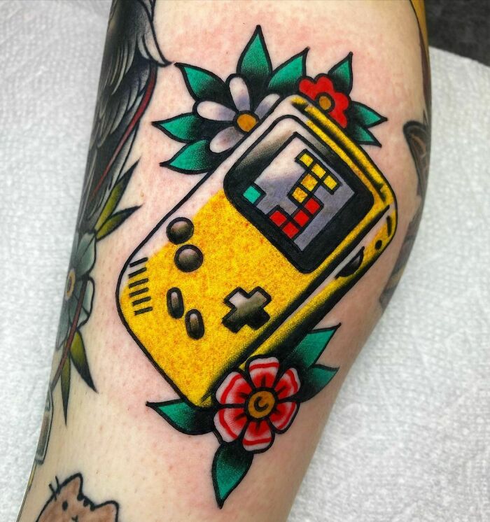 Tattoo of a yellow handheld Tetris video game console with floral designs.