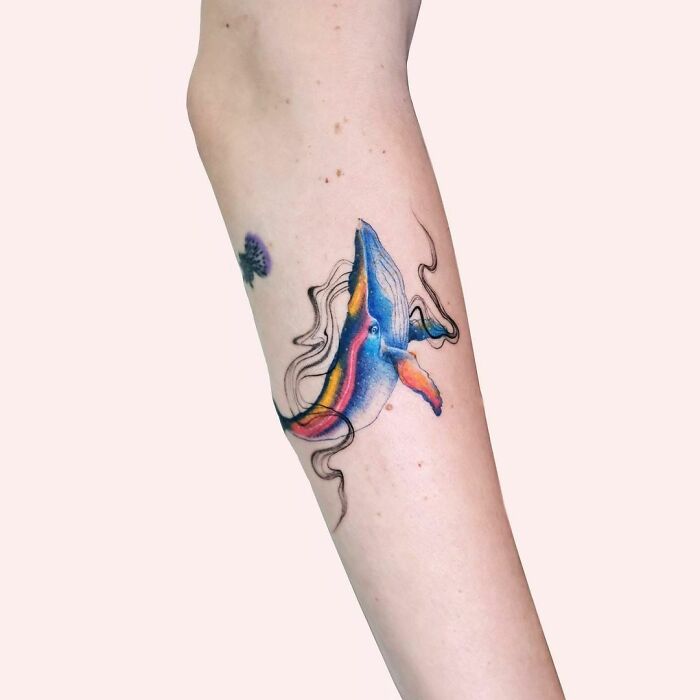 Colorful abstract whale tattoo on a person's forearm, showcasing artistic self-expression.