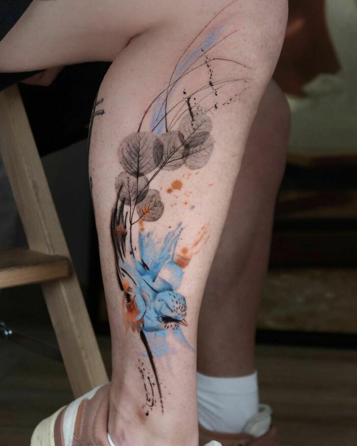 Abstract tattoo design with blue and orange ink on leg, showcasing creativity and self-expression.