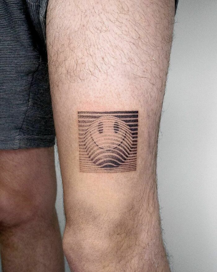 Abstract tattoo of a smiley face with striped pattern on a person's leg.