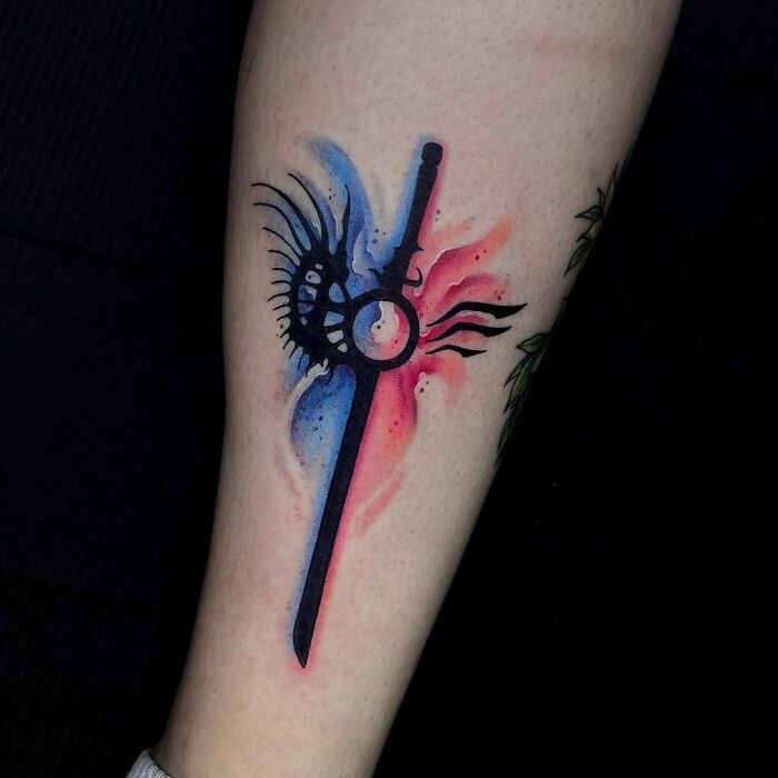 Devil May Cry video game tattoo featuring a sword design with red and blue watercolor effects on arm.