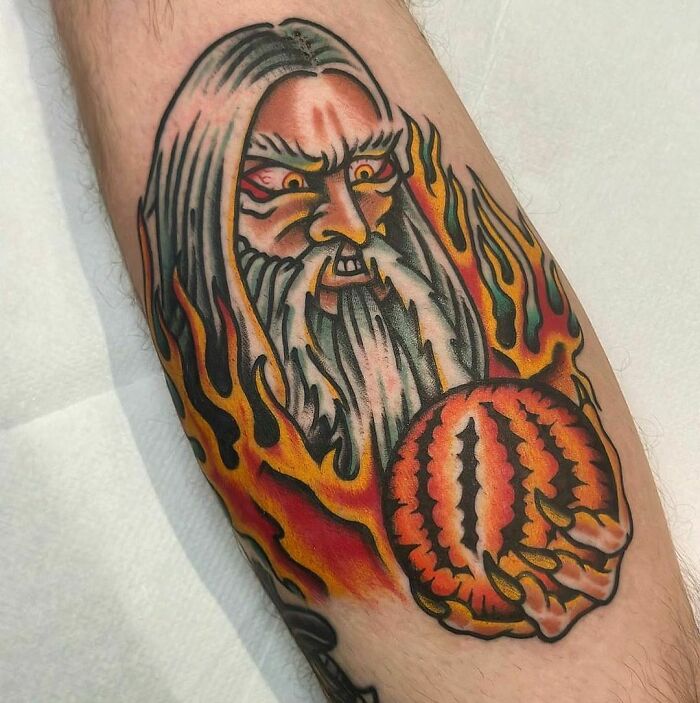 Tattoo of a wizard with fiery hair and a glowing orb, inspired by Lord of the Rings themes.