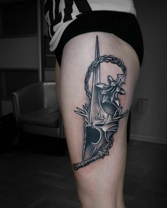 Lord of the Rings tattoo on a thigh, featuring a detailed design of a helmet with spikes and chain elements.