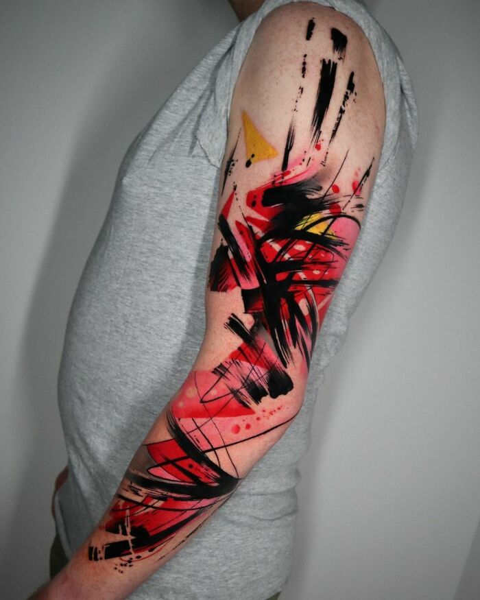 Abstract tattoo design with red and black brushstrokes on a person's arm, showcasing artistry and self-expression.