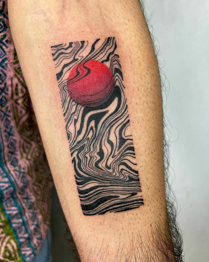 Abstract tattoo of swirling patterns with a red circle on an arm.