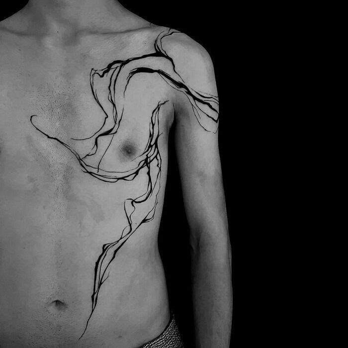Abstract tattoo with flowing lines on a man's chest and shoulder, showcasing artistry and self-expression.