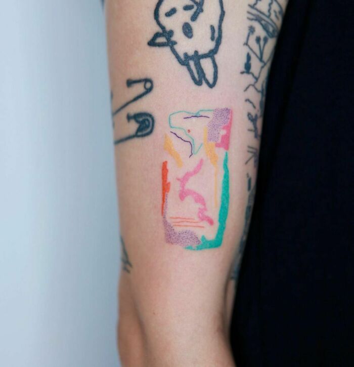 Abstract tattoo with colorful geometric shapes and doodles on an arm, showcasing artistry and self-expression.