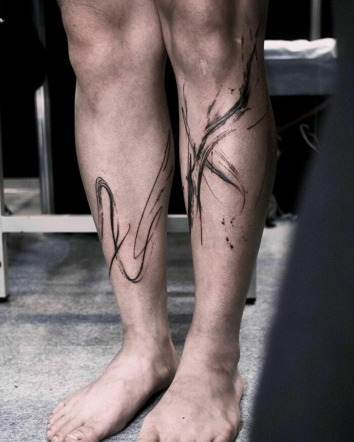 Abstract tattoo design on legs, showcasing artistry and self-expression with bold black strokes.