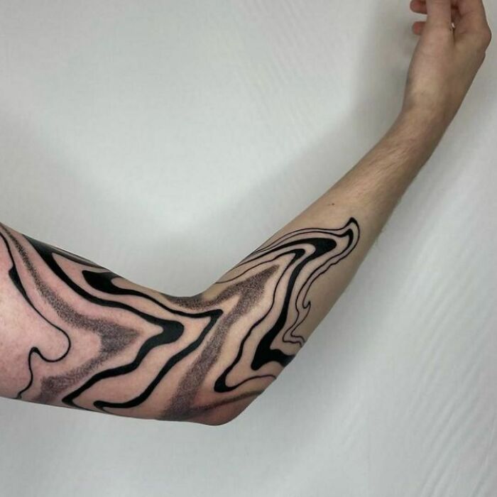 Arm with an abstract tattoo design, showcasing artistry and self-expression in a fluid black pattern.