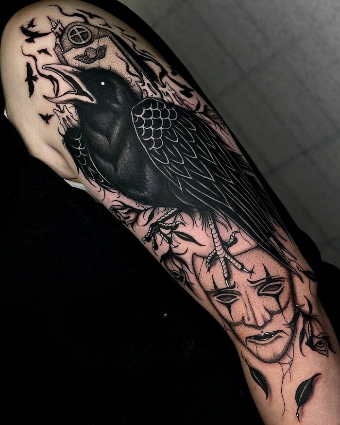 Gothic tattoo of a black raven on an arm with intricate detailing, featuring a mask below.