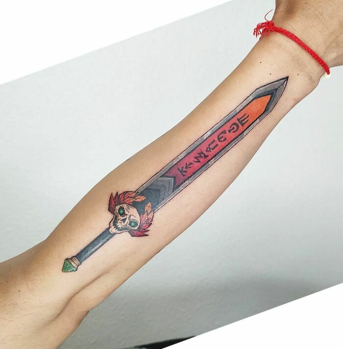 Sword-themed Hades video game tattoo on arm, featuring a skull and runic designs.