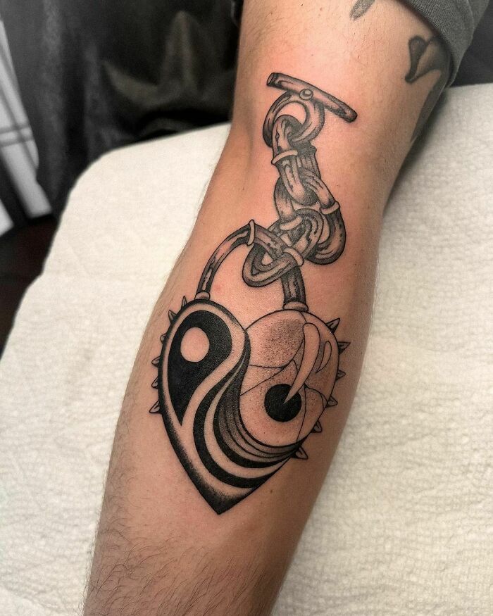 Intricate yin yang tattoo with heart and chain design on a forearm, symbolizing life's duality.