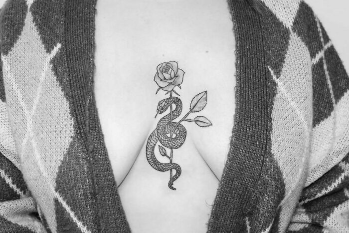 Snake tattoo with a rose on back, black and white, displayed between a sweater's opening.