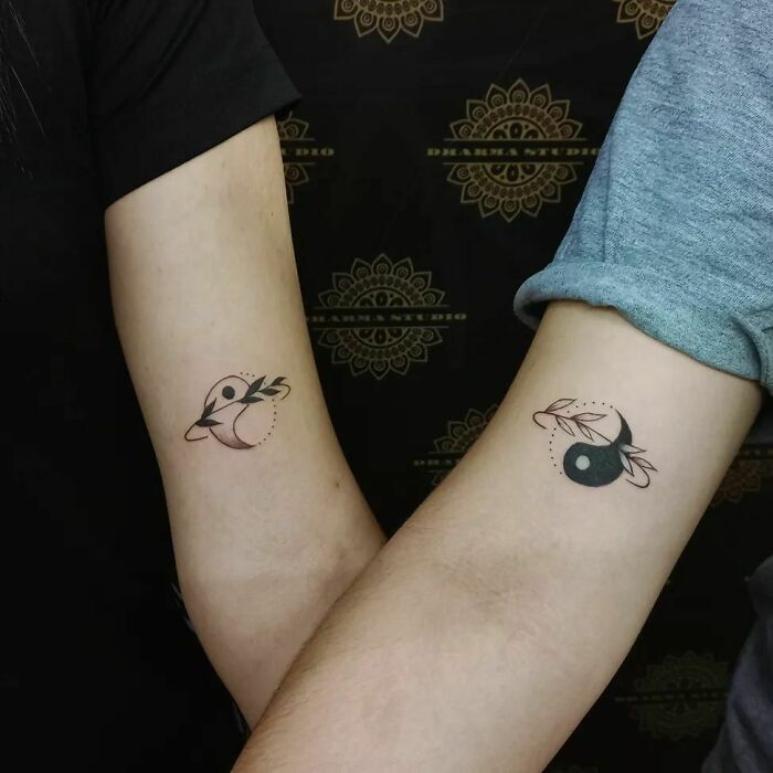 Two arms with matching yin yang tattoos, each featuring leaf designs, symbolizing duality and harmony.
