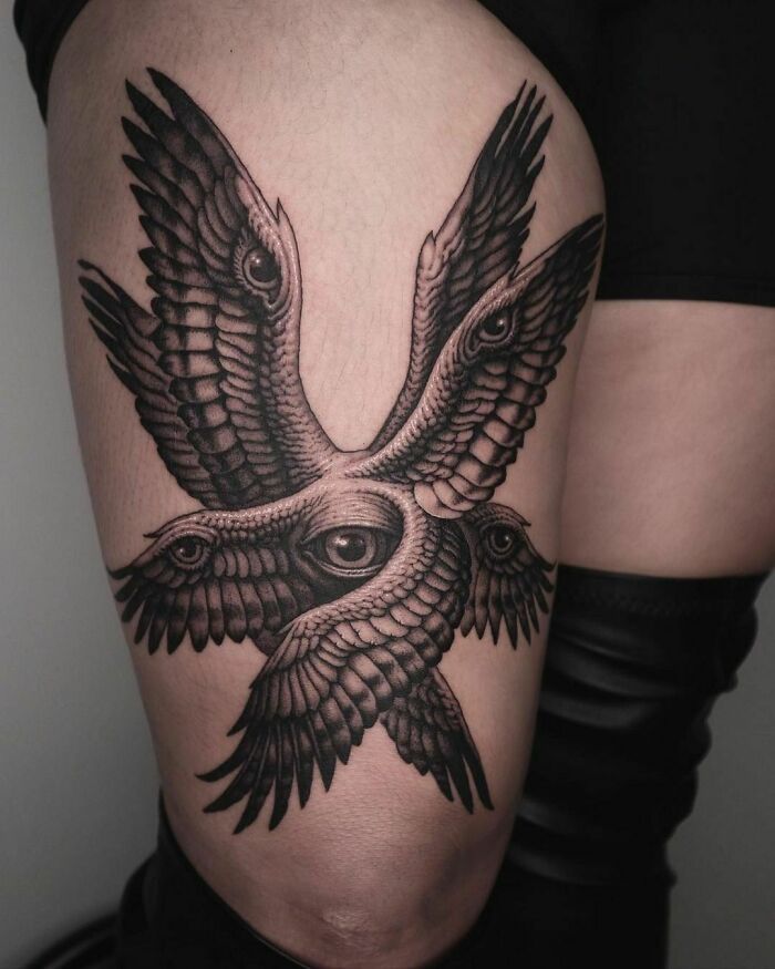 Abstract tattoo design featuring intricate patterns of wings and eyes on a person's thigh.