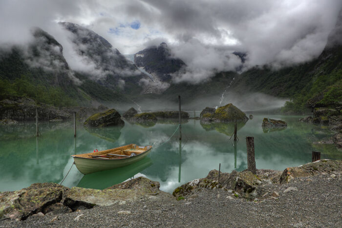 Mist-covered mountains surround a calm lake with a wooden boat, showcasing one of the best pictures chosen by the Wikimedia Commons community.