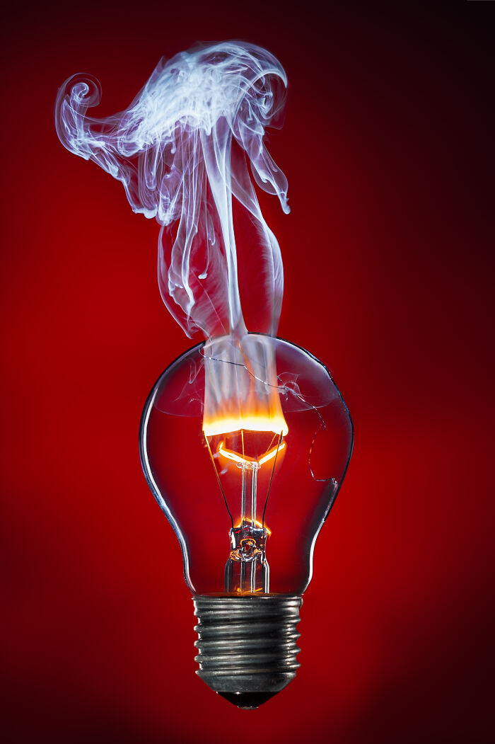Burning filament inside a broken light bulb with smoke rising, featured in best pictures community collection.