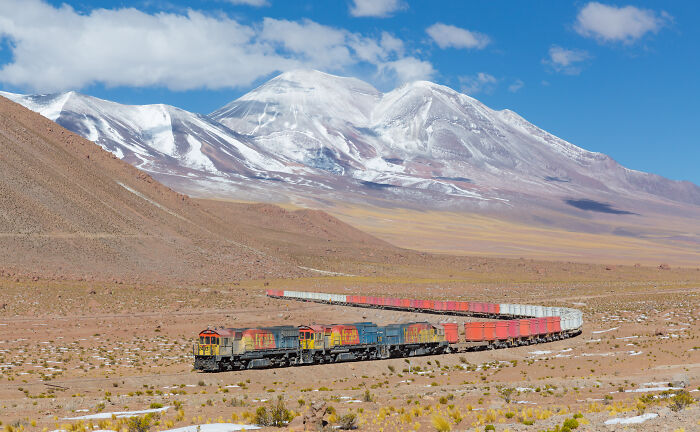 Colorful freight train traveling through desert landscape with snow-capped mountains in the background, best pictures from 2006-2022.