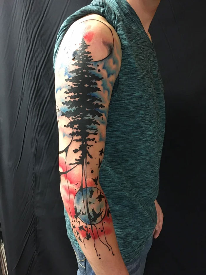Abstract tattoo with trees and celestial designs on a person's arm, combining artistry and self-expression.
