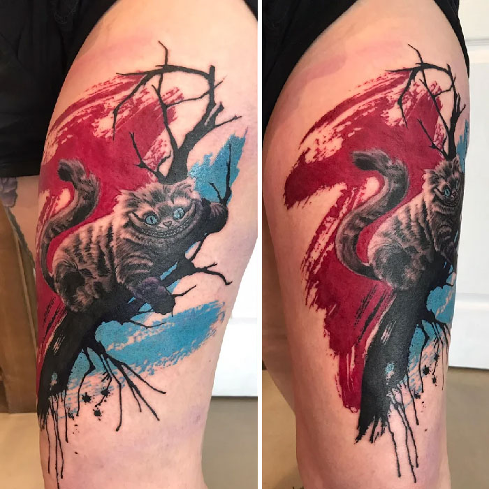 Abstract tattoo of a Cheshire cat on a branch with red and blue paint splashes.
