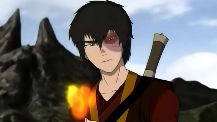 Zuko from Avatar The Last Airbender concentrating as he plays with fire against a rocky mountainous background.