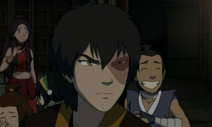 Zuko from Avatar The Last Airbender looking angry and intense in a dimly lit scene with friends in the background.