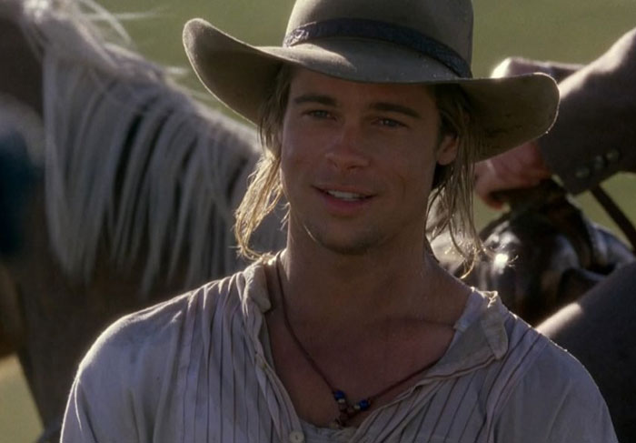 Actor in a vintage setting, wearing a cowboy hat and light shirt, standing outdoors.