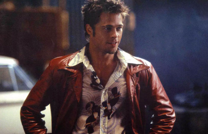 Young actor in a patterned shirt and brown jacket, drawing attention to age with a confident expression.