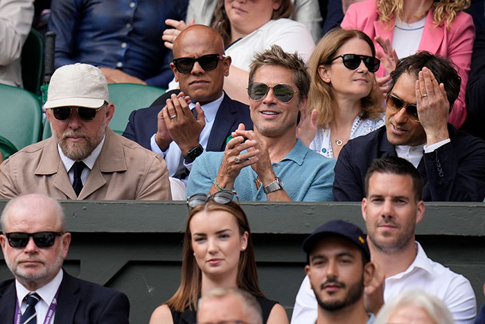 "Brad Pitt in sunglasses and a blue shirt, sitting among fans at Wimbledon, drawing surprise over his age.