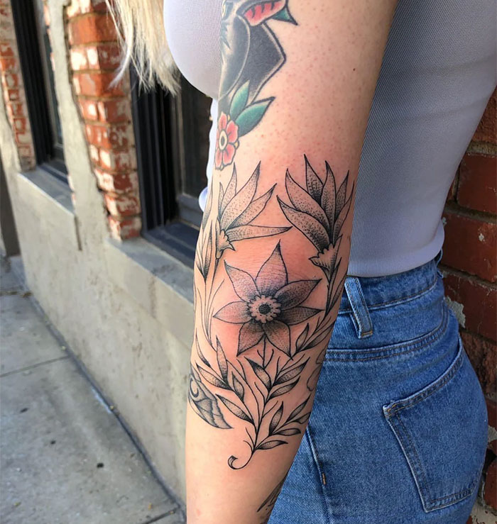 Floral elbow tattoo on a woman's arm, showcasing intricate black and gray designs.