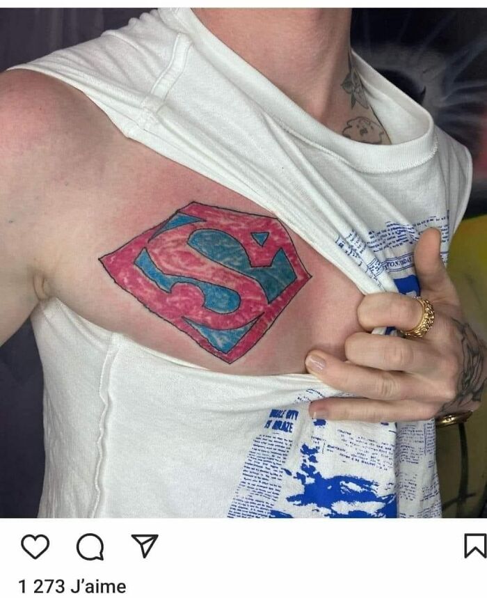 Close-up of a humorous Superman logo tattoo on a person's chest, revealed by lifting their shirt.