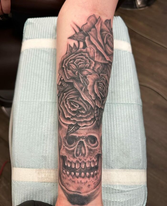 A tattoo of a skull with roses on a forearm, styled in black and gray, humorously considered one of the worst tattoos.