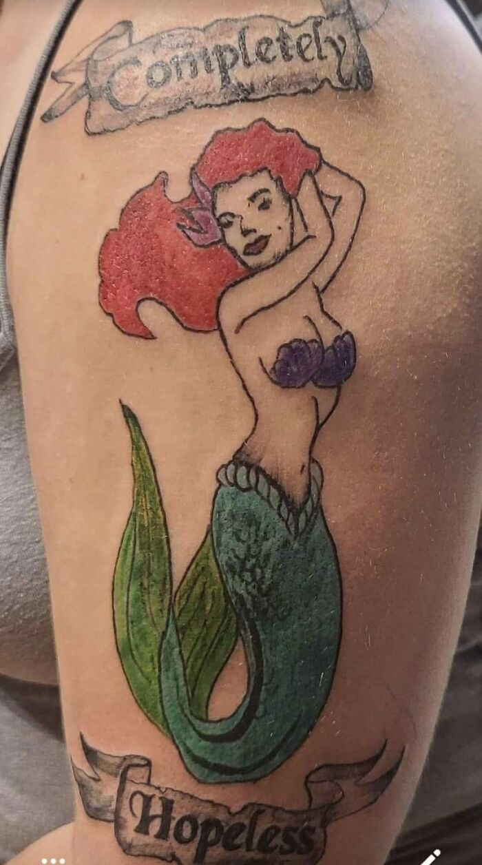 Funny tattoo of a mermaid with banners saying "Completely Hopeless" on an arm.
