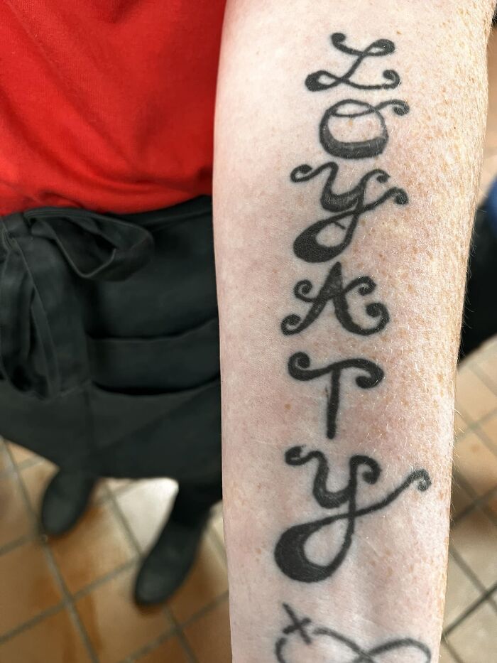 Arm tattoo spelling "LOYALTY" in a decorative script.